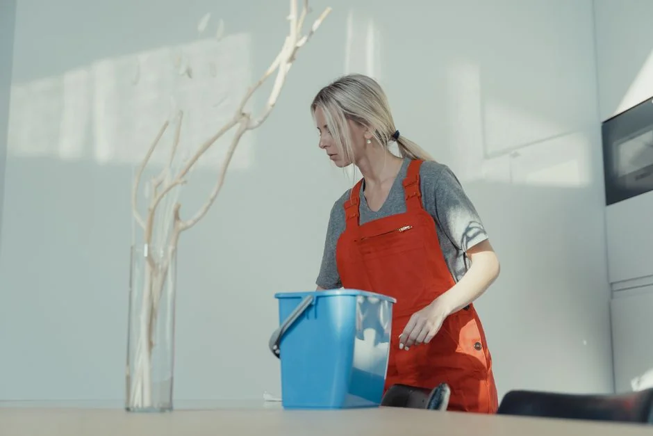 Two women wearing red overalls vacuuming and sweeping a contemporary living room.